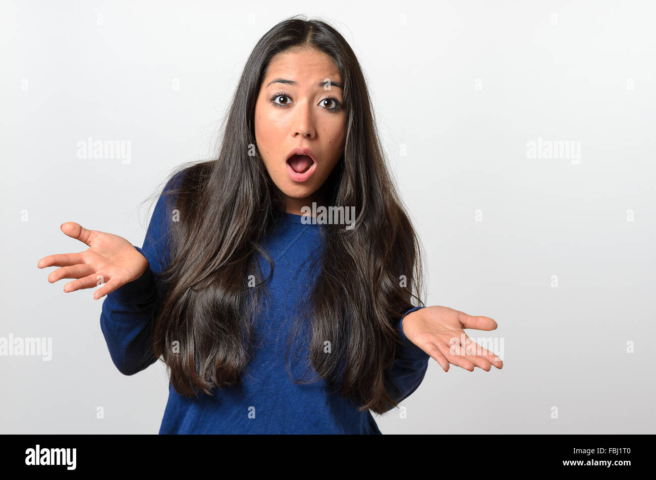 Young woman shrugging her shoulders and gesturing with her hand with her mouth open in protest as she shows her ignorance or inn Stock Photo