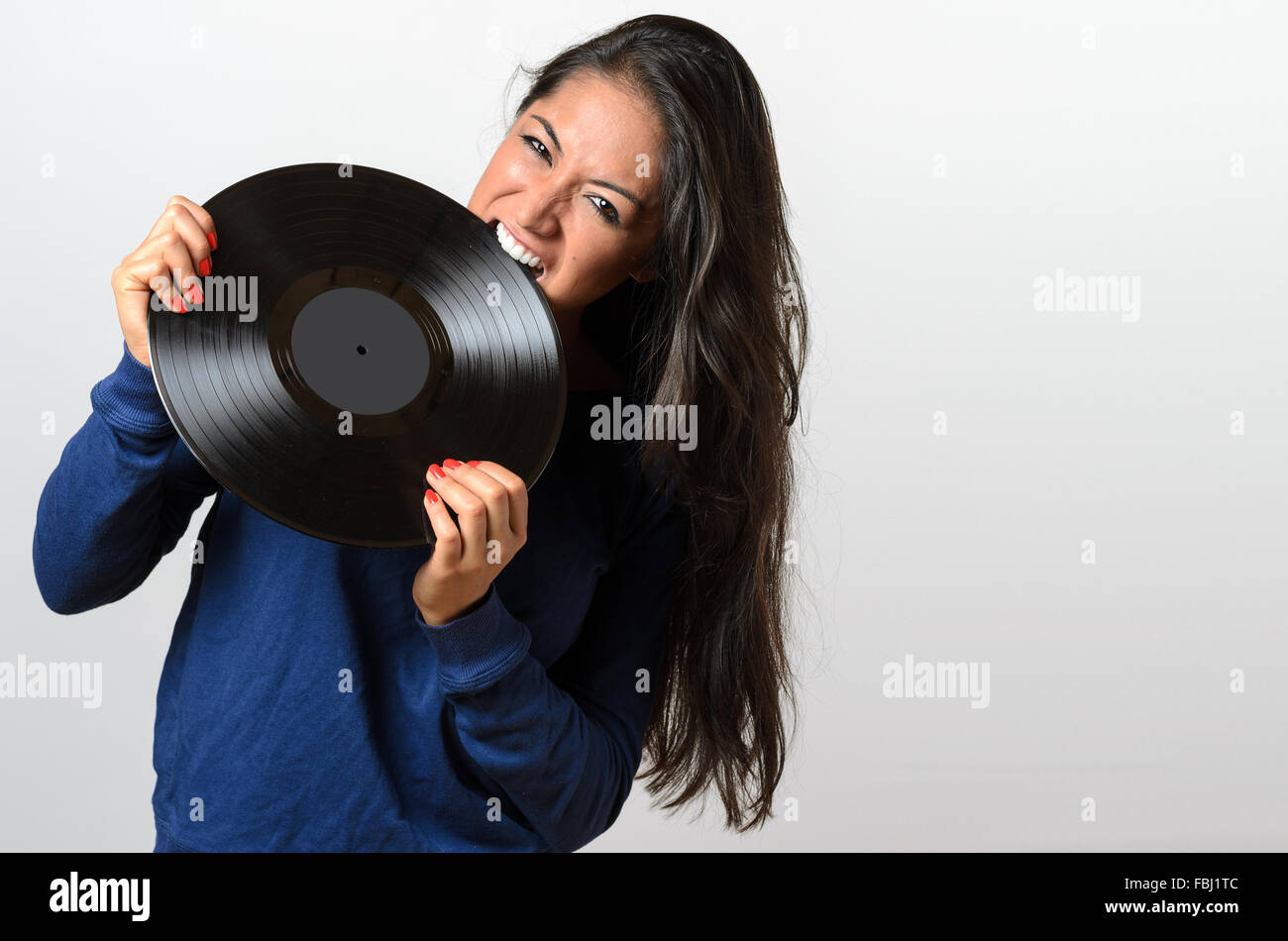 Frustrated attractive young woman biting on a vinyl record with a snarl and frown of anger Stock Photo