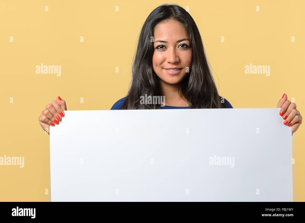 Smiling attractive young woman holding a blank white sign with copy space for your text that she is holding in front of her ches Stock Photo
