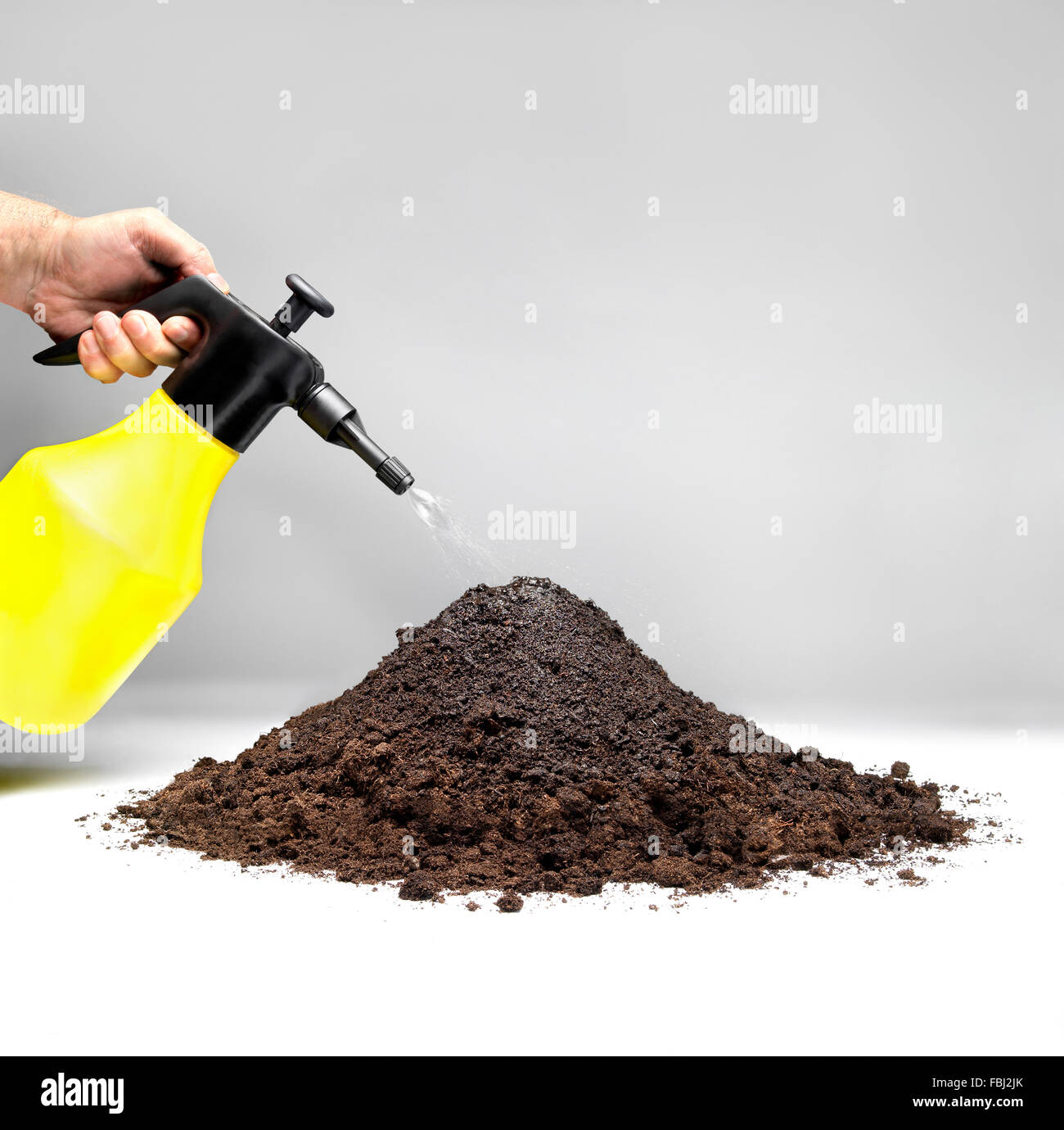 Watering a pile of soil with a sprinkler against gray background. Stock Photo