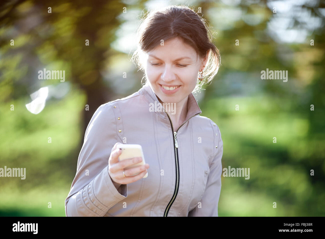 Portrait of happy smiling caucasian woman in park siting on the bench, using mobile phone, messaging Stock Photo