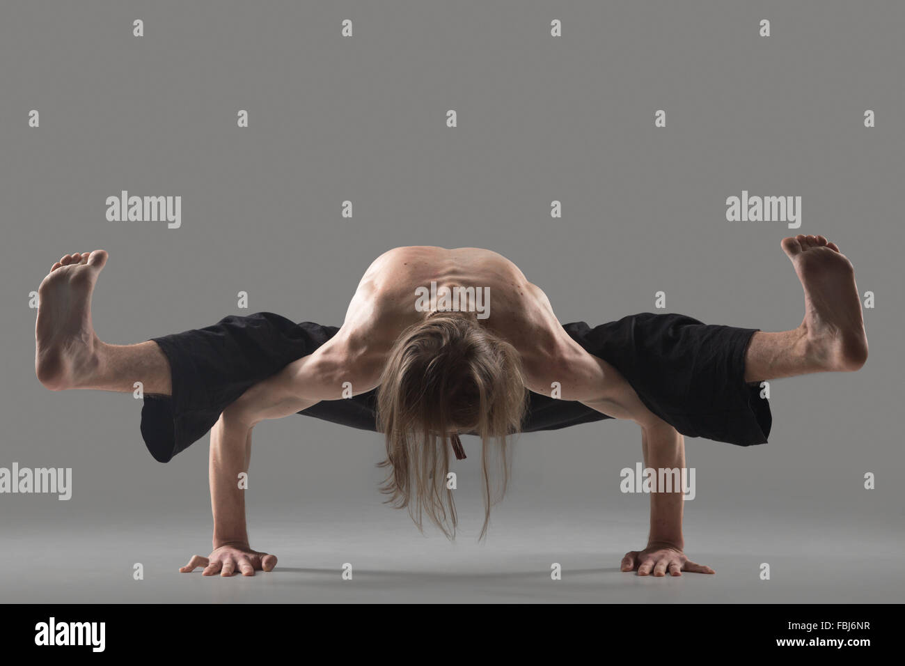 Sporty young man in black trousers doing arm balance exercise, variation of Firefly posture, strengthening the wrists, forearms Stock Photo