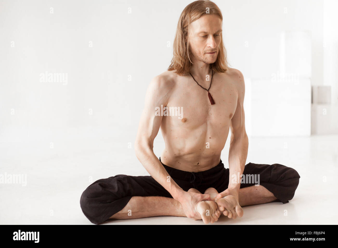Sporty young man in black trousers sitting in baddha konasana posture (purna titli, bound angle, cobbler, butterfly pose) Stock Photo