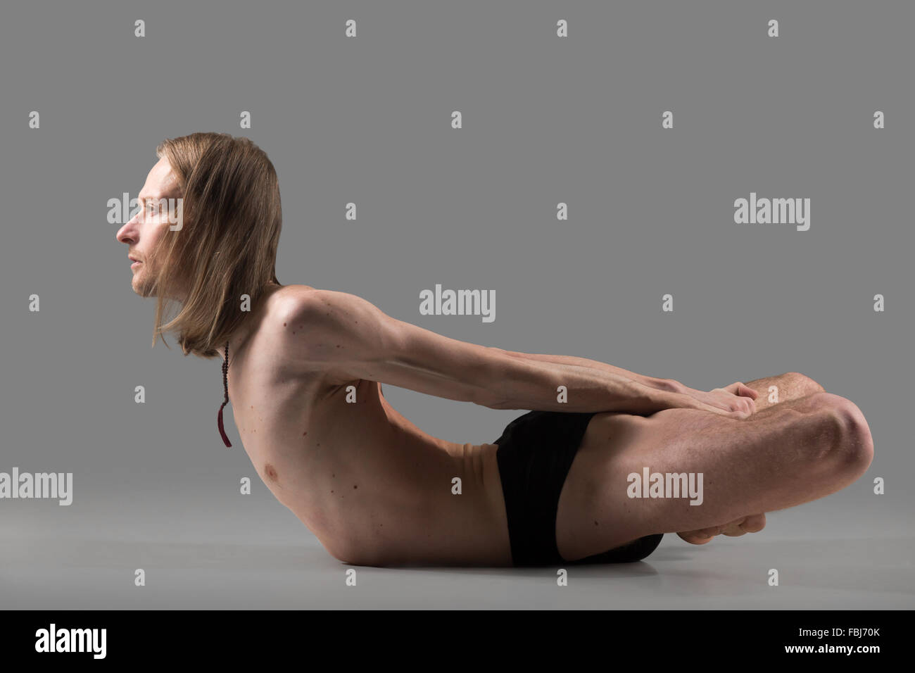Sporty muscular young yogi man doing backbend exercise, Viparita Baddha Matsyasana, studio shot on dark background, side view, f Stock Photo