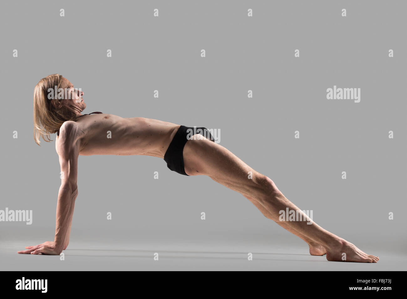 Sporty muscular young yogi man doing variation of Purvottanasana, Upward Plank posture, studio shot, exercise for abs and spine, Stock Photo