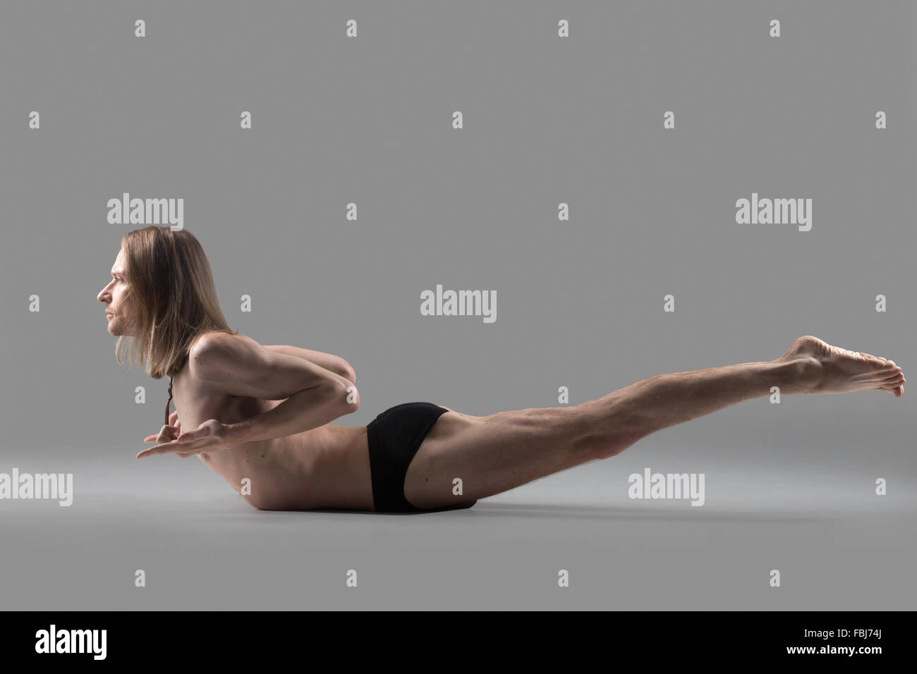 Sporty muscular young yogi man doing variation of Salabhasana, Locust Pose, Double Leg Kicks, studio shot on dark background, si Stock Photo