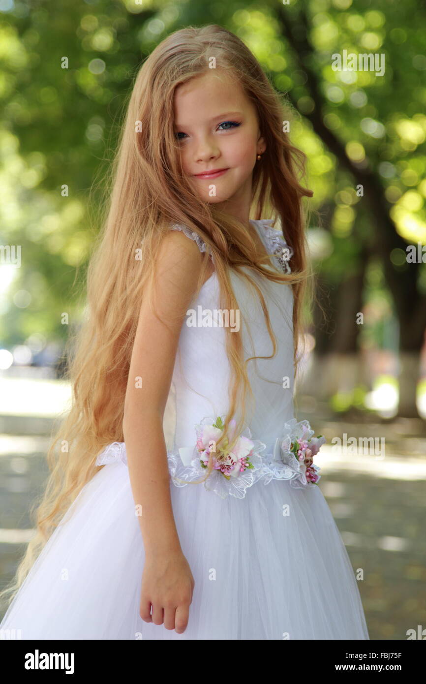 European blonde smiling little girl in a white ball gown in the summer park outdoors Stock Photo