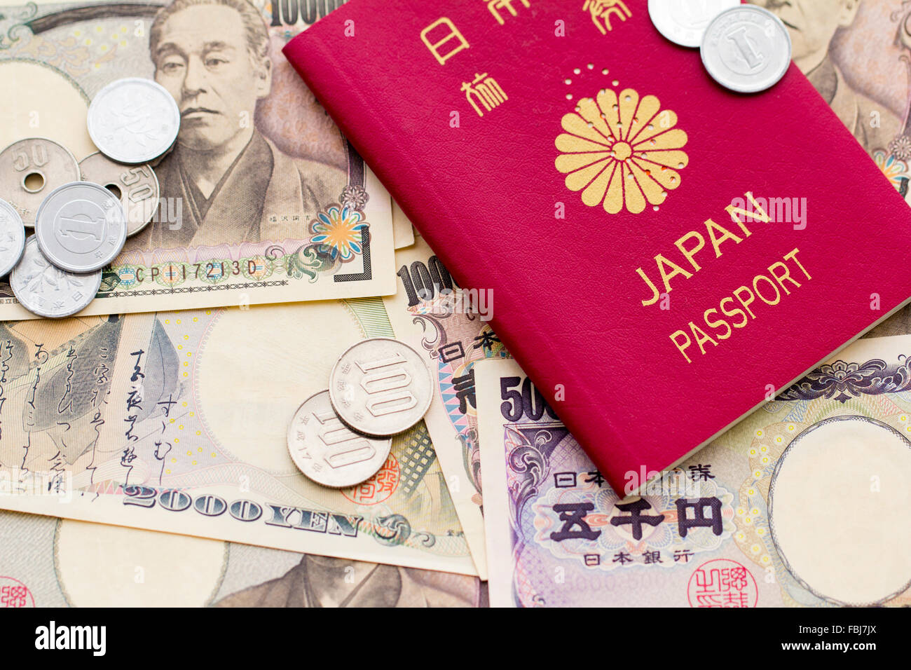 Travel, money and currency. Red Japanese passport on top of scattered various domination Japanese yen banknotes and some small change, coins, on top. Stock Photo