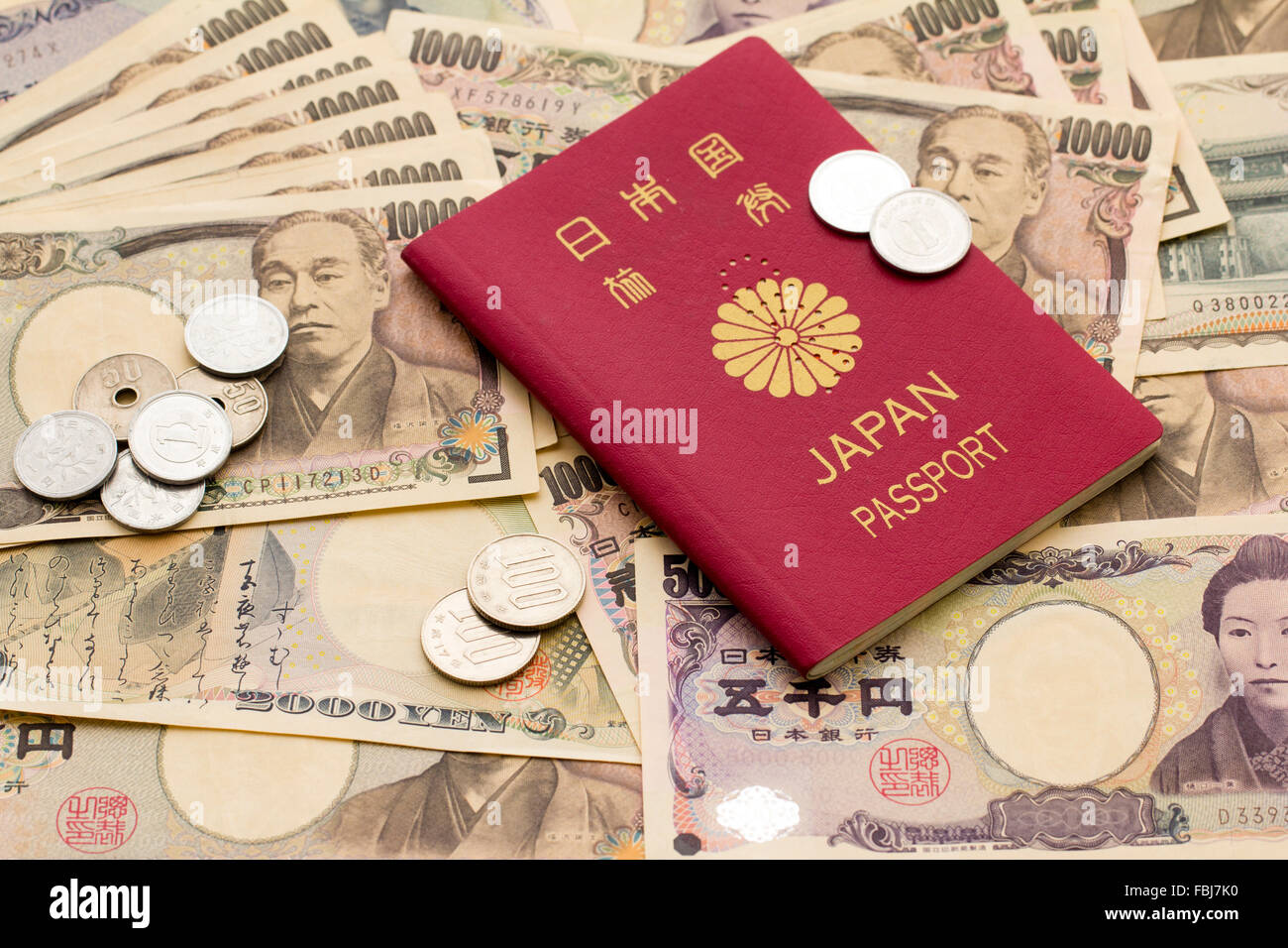 Travel, money and currency. Red Japanese passport on top of scattered various domination Japanese yen banknotes and some small change, coins, on top. Stock Photo