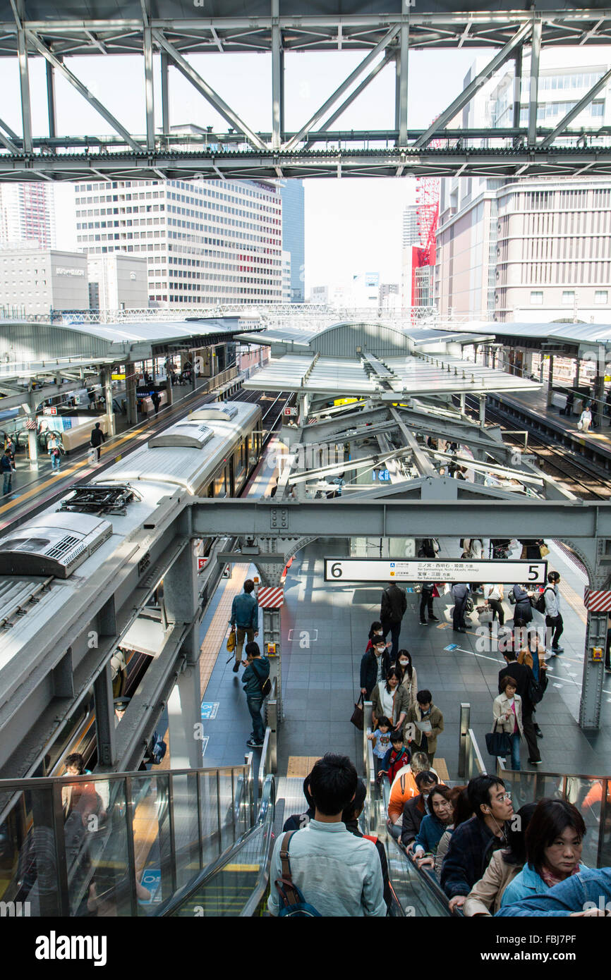 Osaka station. Overhead view along platforms 5 and 6 with escalators, one going up packed with people, commuter train departing. Daytime. Stock Photo
