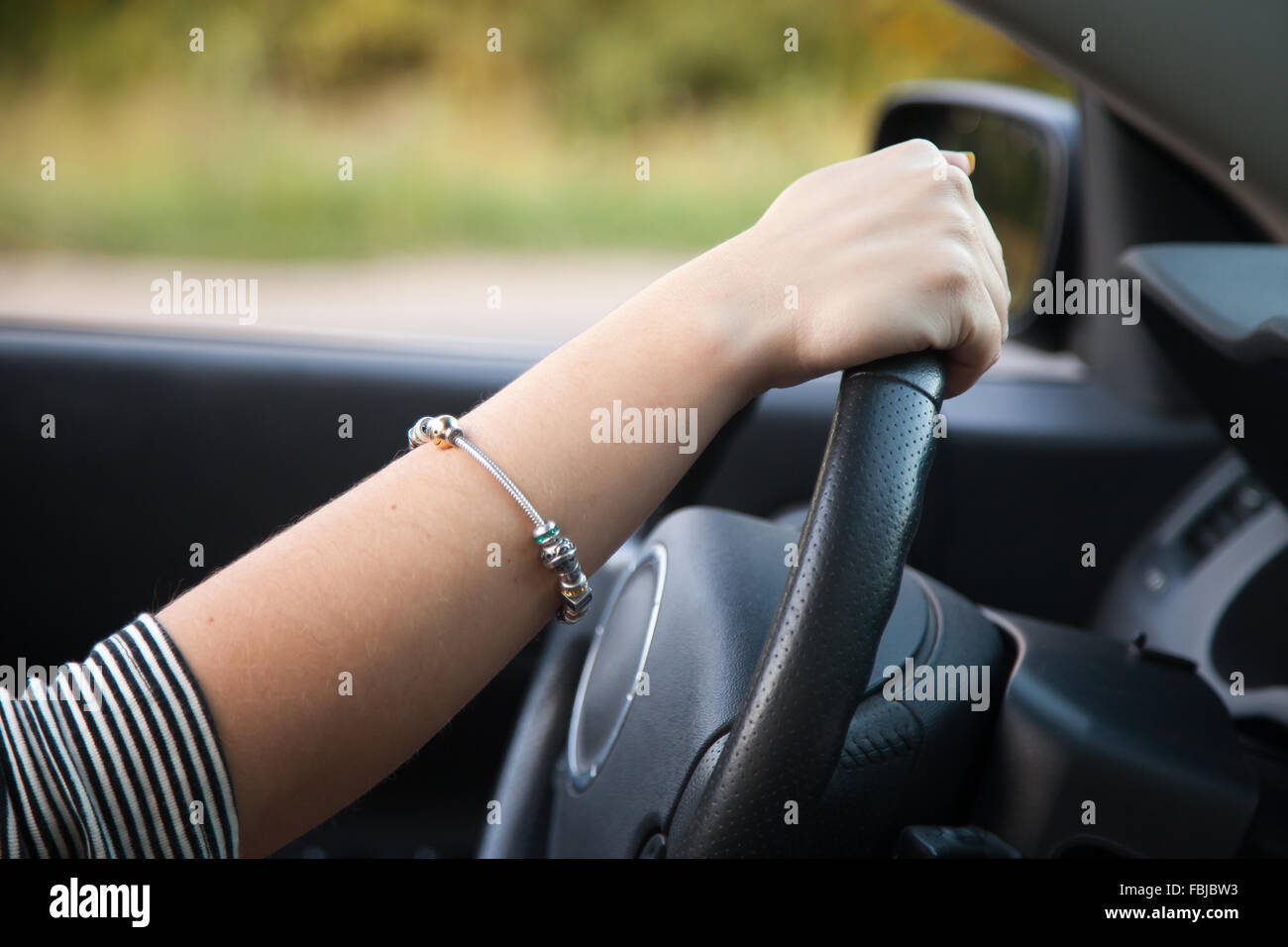 Close up of female hand holding black steering wheel, young woman driving car Stock Photo