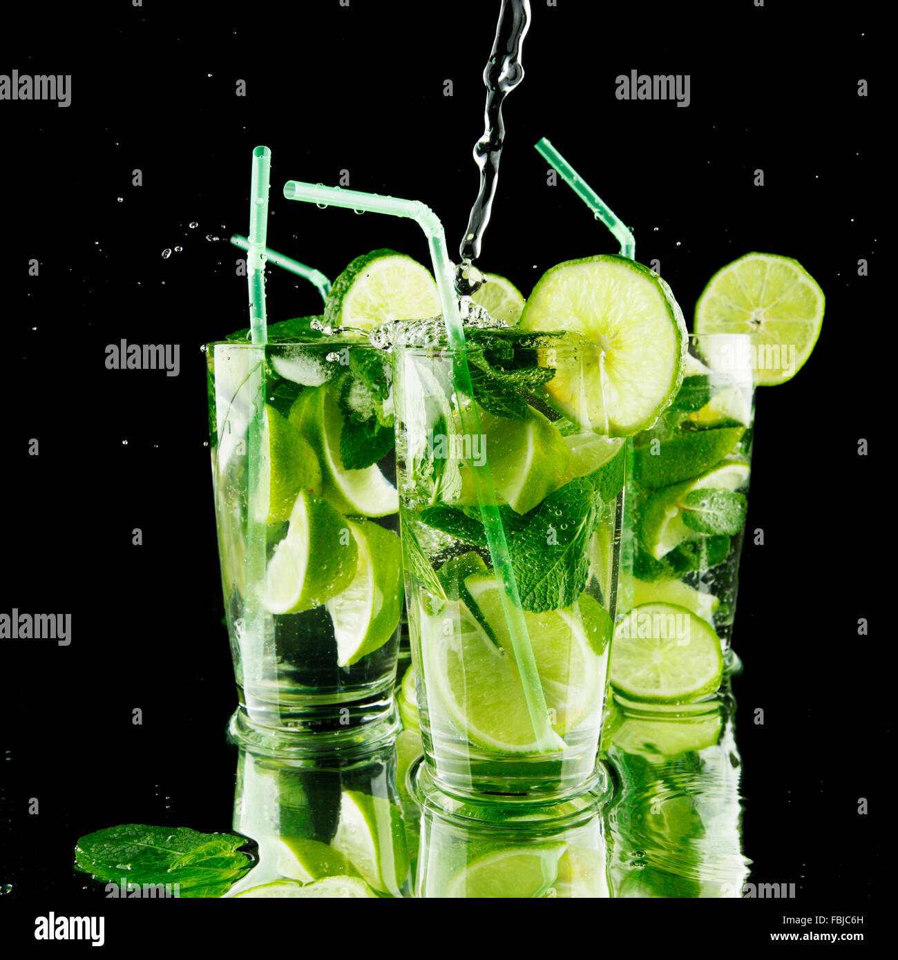 Pouring fresh mojito cocktail in glasses isolated on black background ...