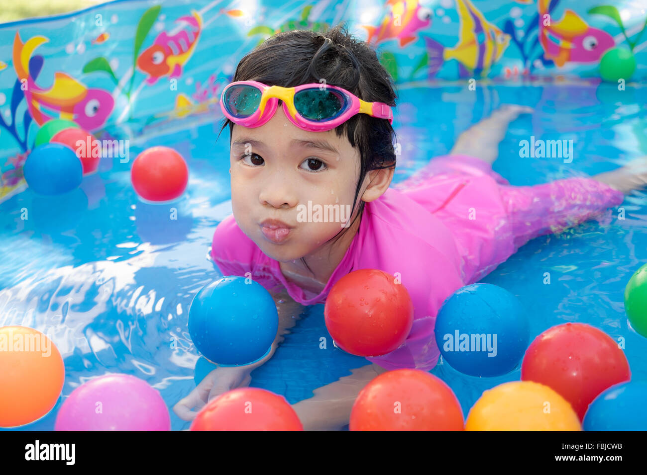 A baby girl in pink suit playing water and balls in blue kiddie pool