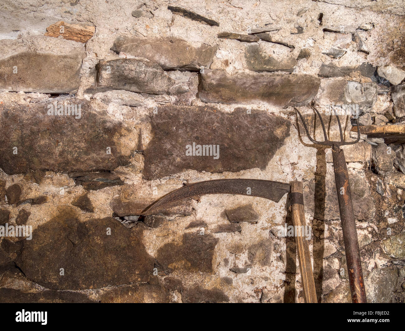 Farm equipment. Old pitchfork and scythe against stone wall Stock Photo Alamy