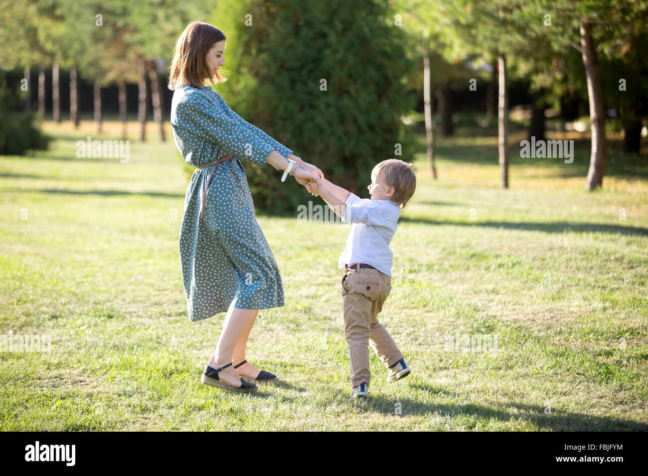 Portrait of happy young mom and her adorable little son playing and dancing together in park in summertime, smiling mother and k Stock Photo