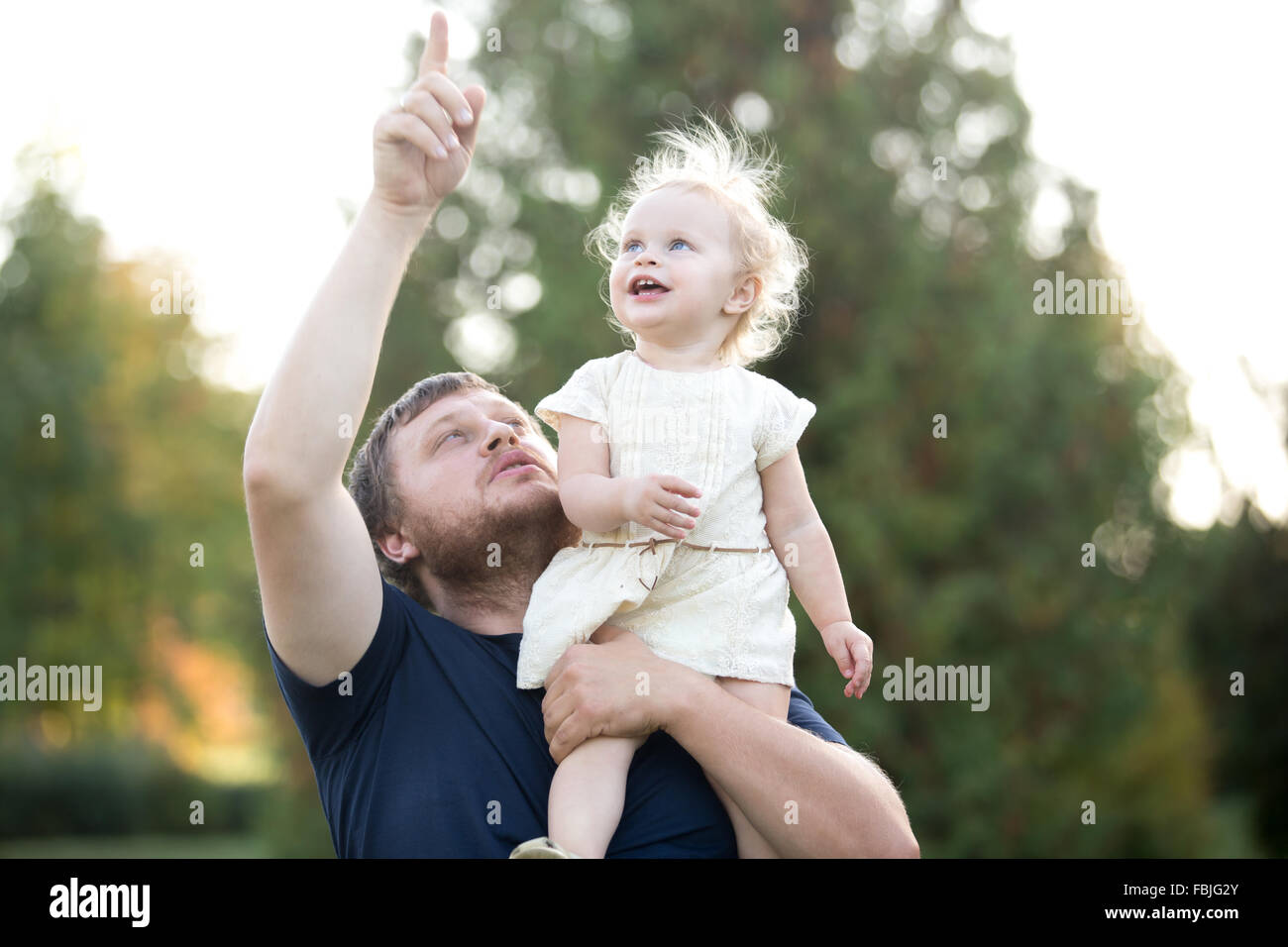 Portrait of happy dad and toddler daughter walking in summer park, having fun together. Father carrying excited kid on shoulder, Stock Photo