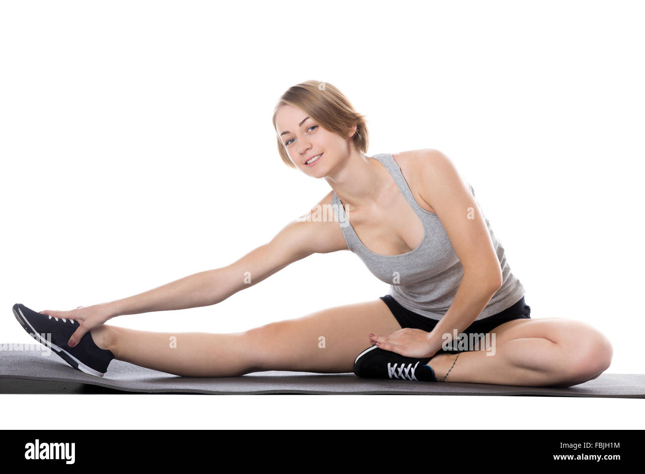 Portrait of young cheerful slim beautiful woman doing fitness exercises on mat, warming up, stretching her legs, full length Stock Photo