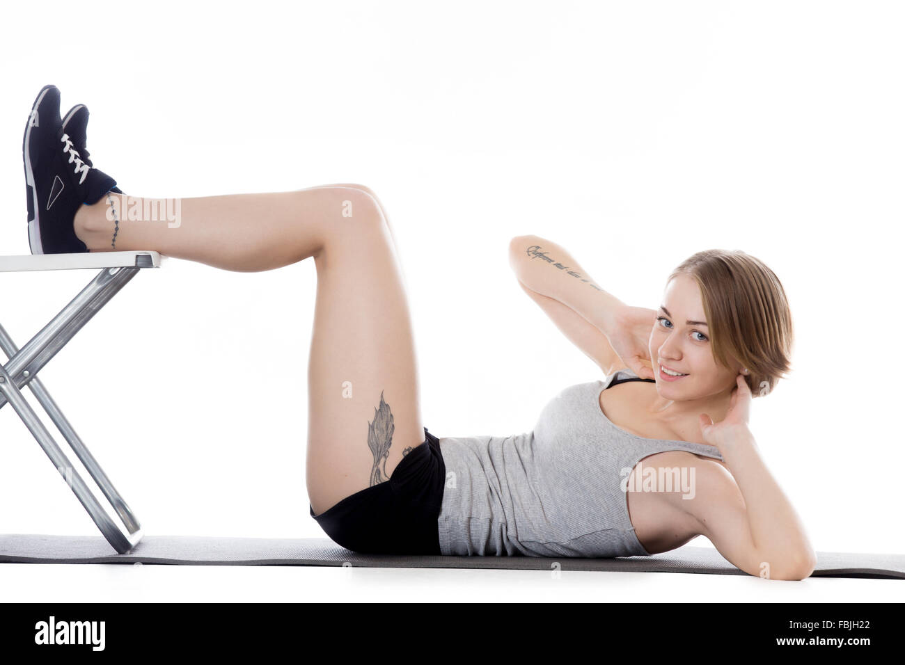 Portrait of young happy slim beautiful woman working out on mat, warming up, doing abdominal crunches with office chair Stock Photo