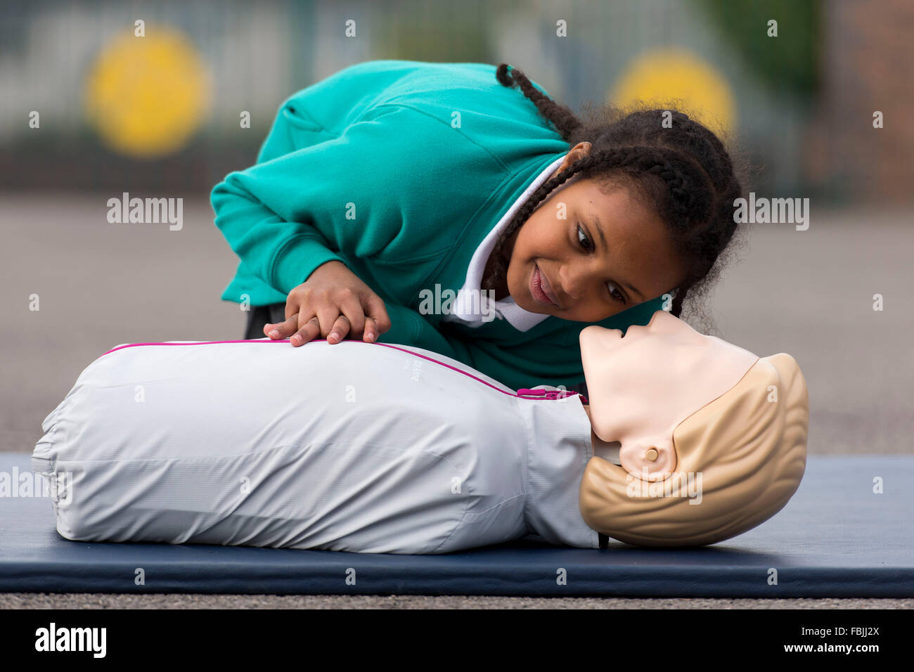 A schoolgirl learns life saving first aid techniques by practicing on a dummy at school. Stock Photo