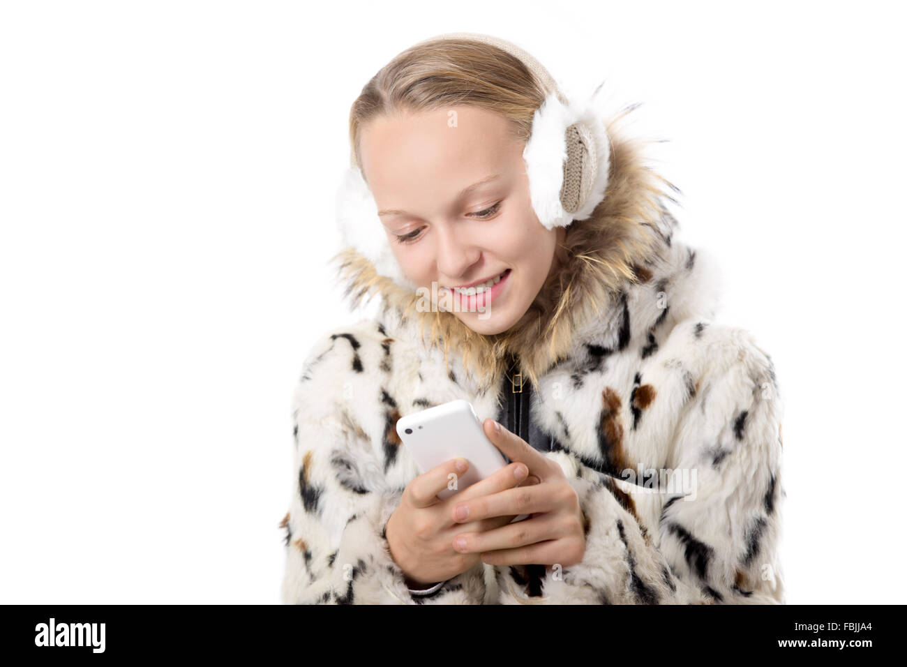 Headshot portrait of happy smiling beautiful casual teenage girl wearing winter coat and earmuffs, holding cellphone in hands Stock Photo