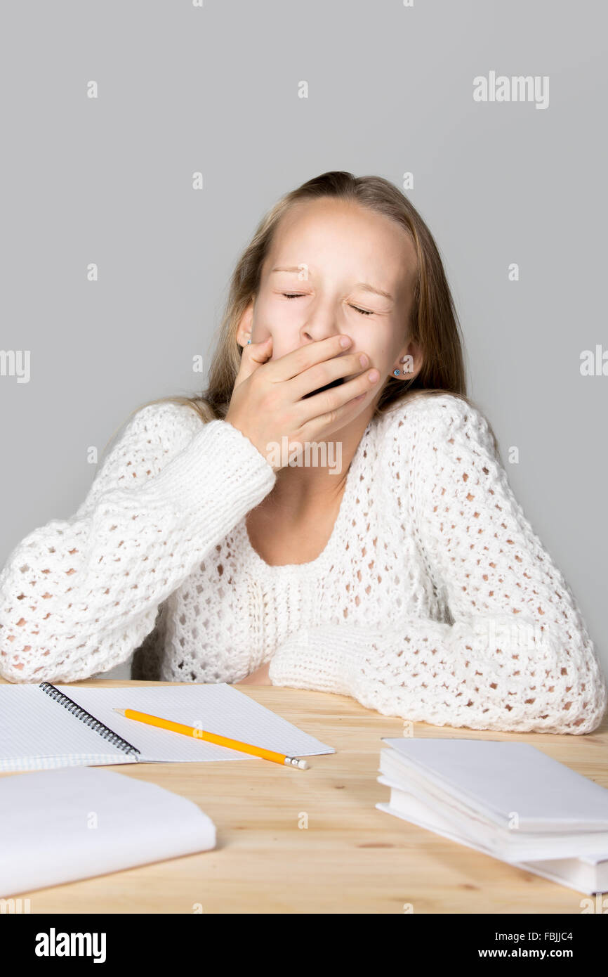 Portrait of sleepy funny beautiful casual girl, sitting at desk, yawning with closed eyes, tired or bored with hard school task Stock Photo