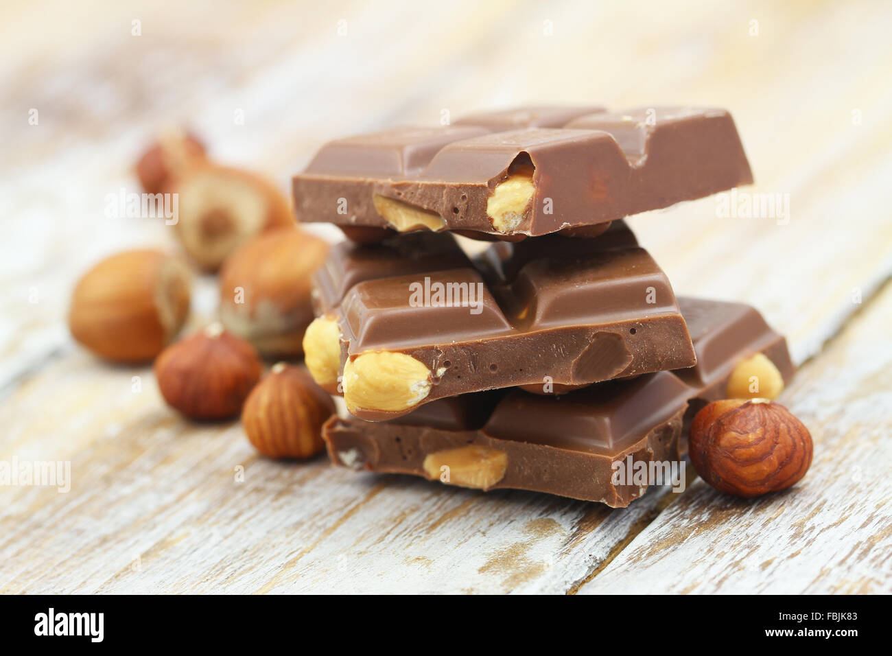 Milk chocolate pieces with whole hazelnuts on rustic wooden surface Stock Photo