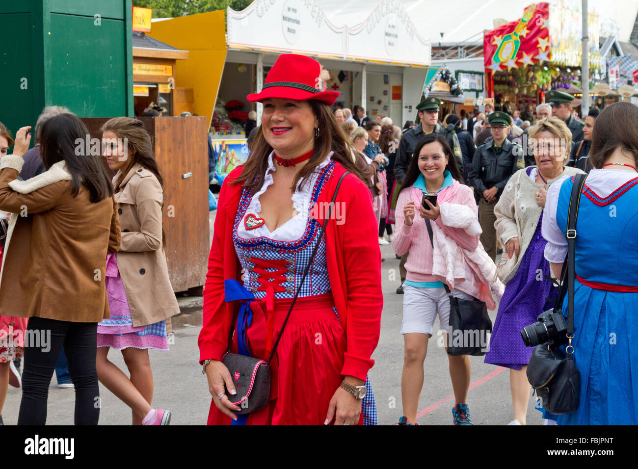 Smiling young women wearing dirndl and Tyrolean hat walking through crowd at Oktoberfest in Munich, Germany Stock Photo