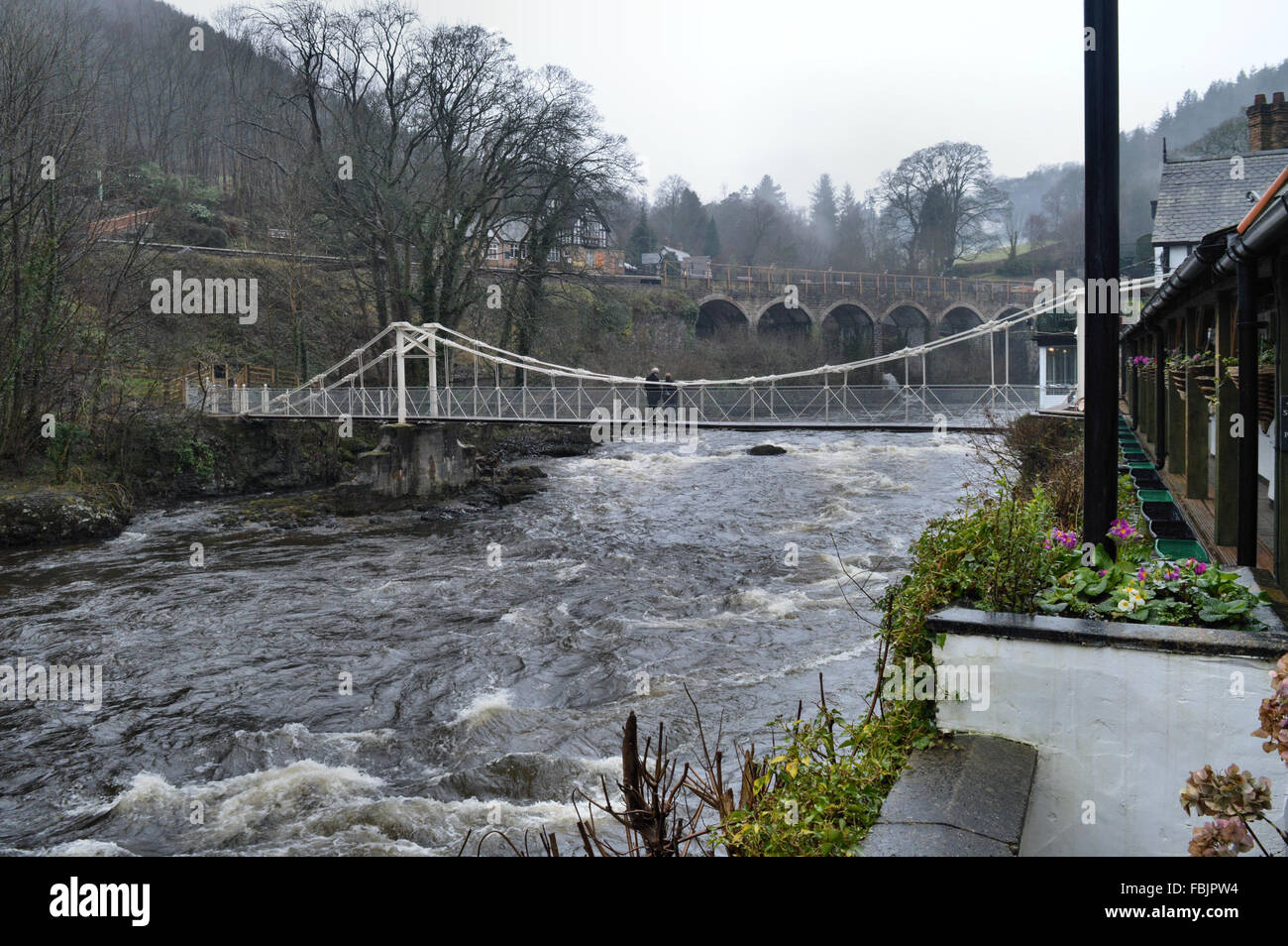 River Dee and two people crossing the chain foot bridge adjoining the Chainbridge Hotel Llangollen Stock Photo