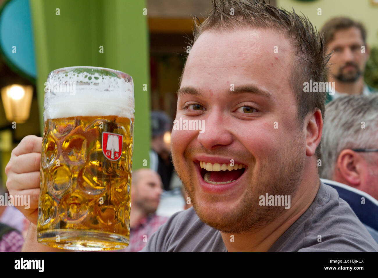 Laughing inebriated young man toasting camera with a mug of beer at Oktoberfest in Munich, Germany. Stock Photo