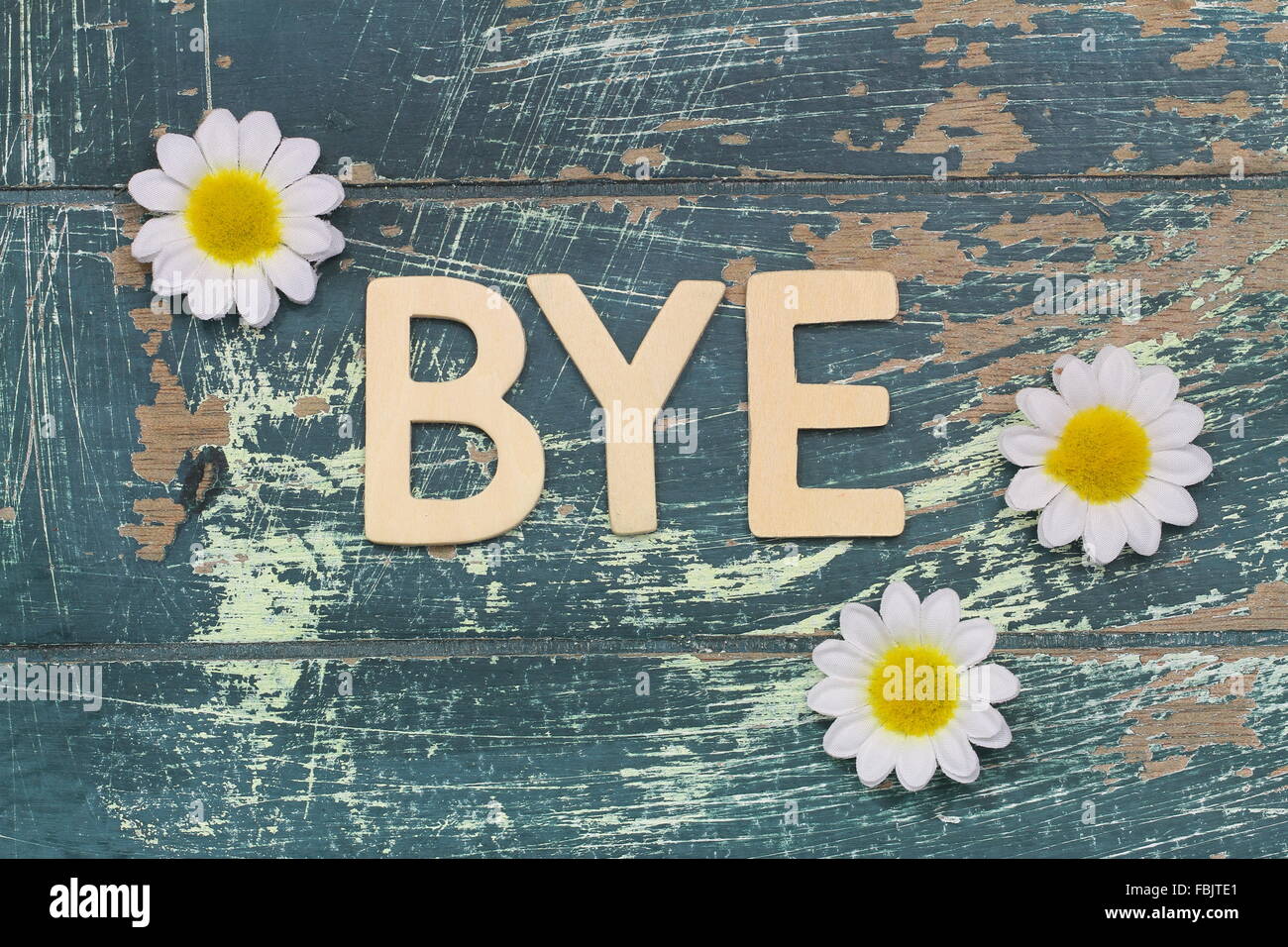 Word bye written with wooden letters on rustic surface and white daisies Stock Photo