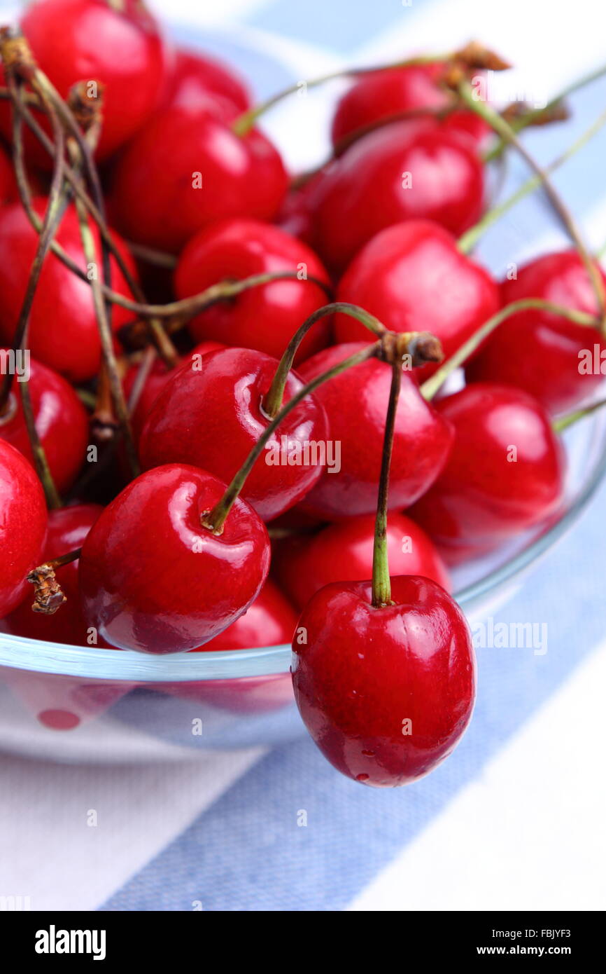 Natural red cherries in a bowl on a blue tablecloth background Stock Photo