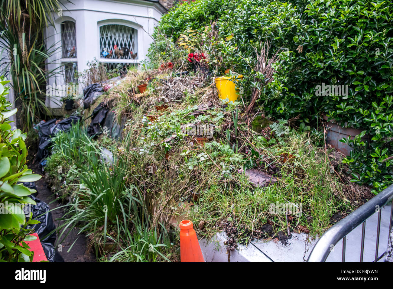 An abandoned car lays under a mountain of grass and refuge in a Dublin city front garden Stock Photo