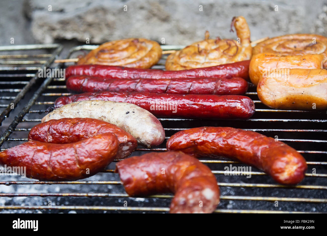 Assortment of grilled sausages and wurst on big grill. Selective focus on the white sausage. Stock Photo