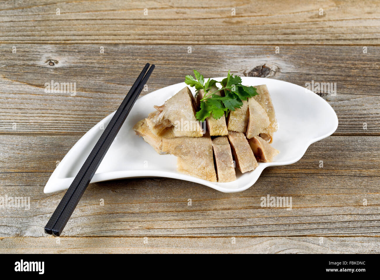 Close up front view of sliced duck meat in small bowl on rustic wood with chopsticks. Stock Photo