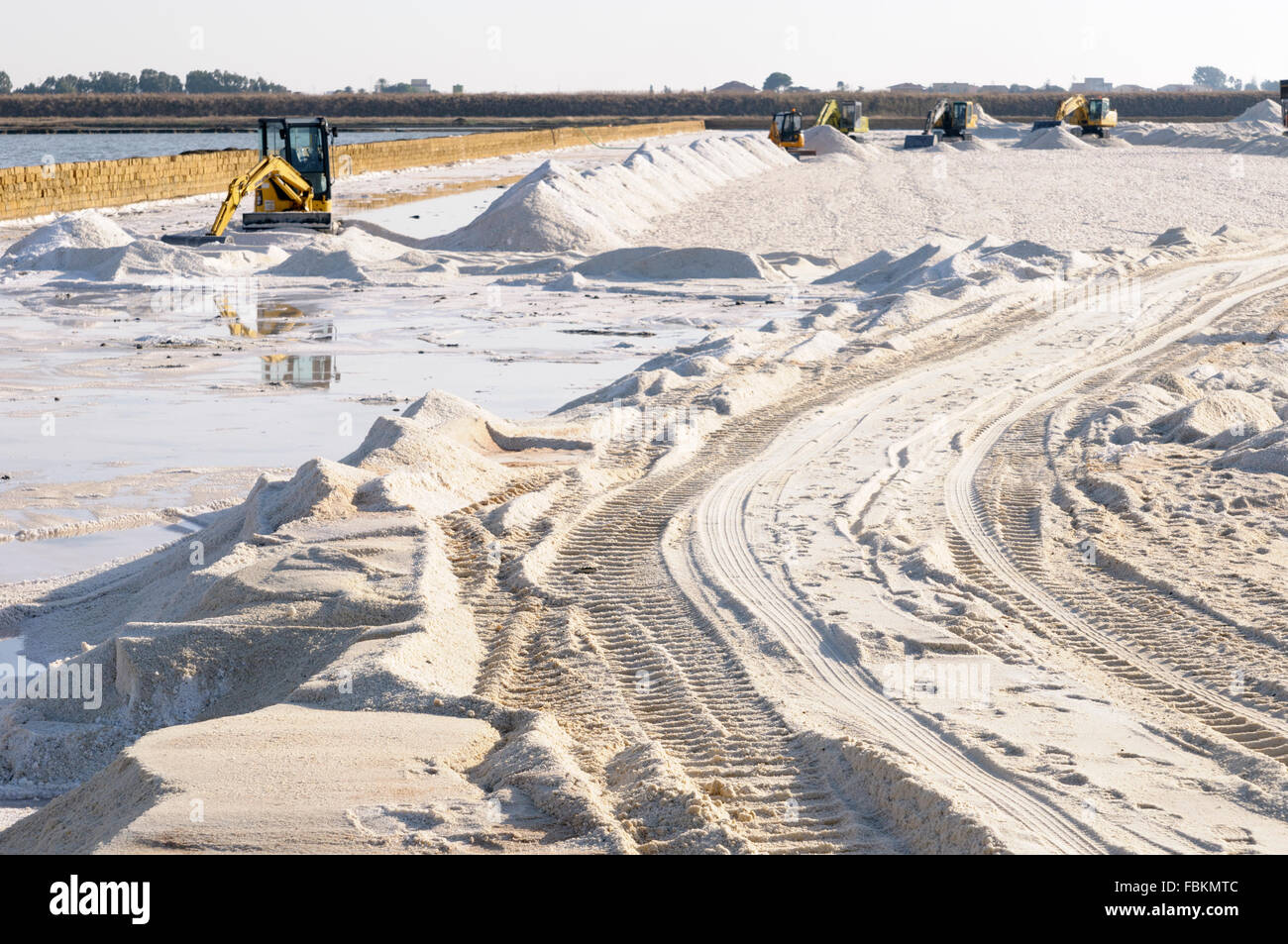 Italy, Sicily, Trapani. A Komatsu crawler excavator harvesting sea salt from a evaporation pond. Stock Photo