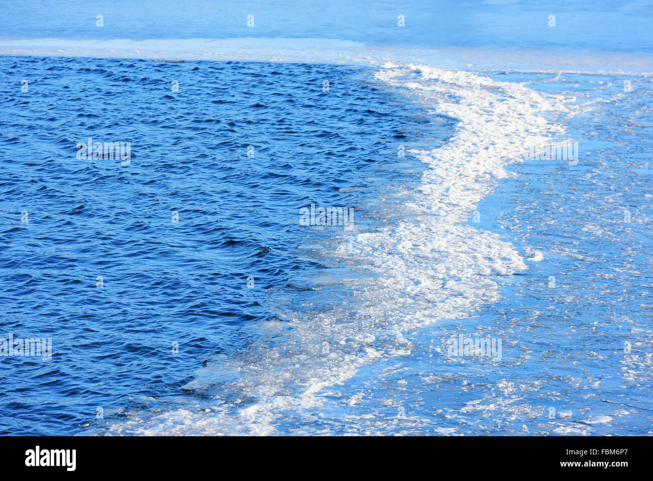 A boundary between calm sea water and ice form a small area of broken ice that almost look like foam. Stock Photo