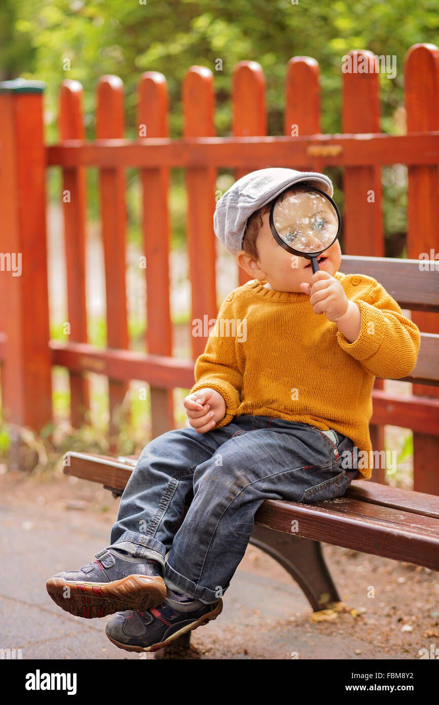 Boy Sitting On Bench Holding A Magnifying Glass Stock Photo
