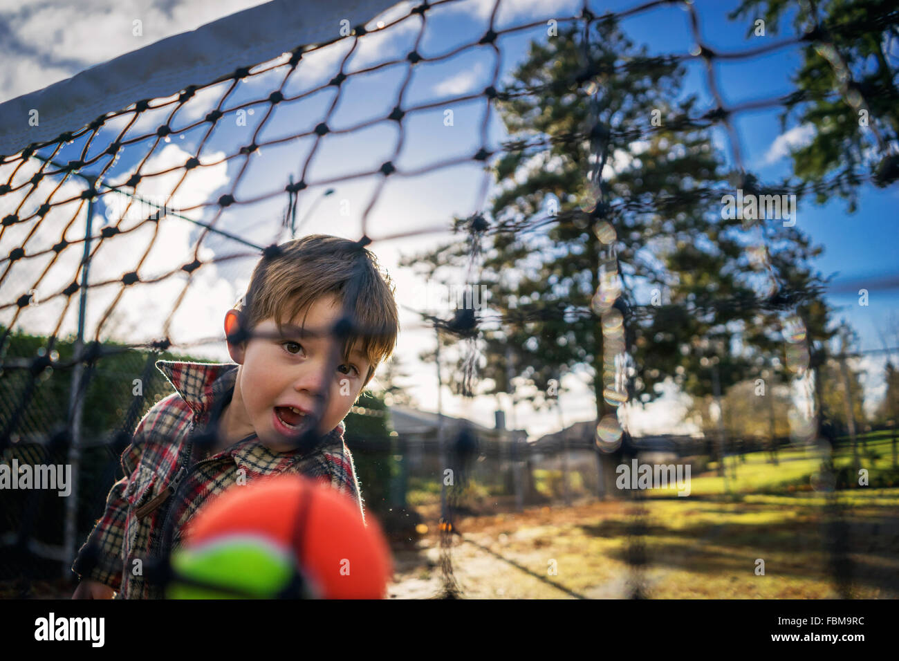 View through a net of a boy throwing tennis ball Stock Photo