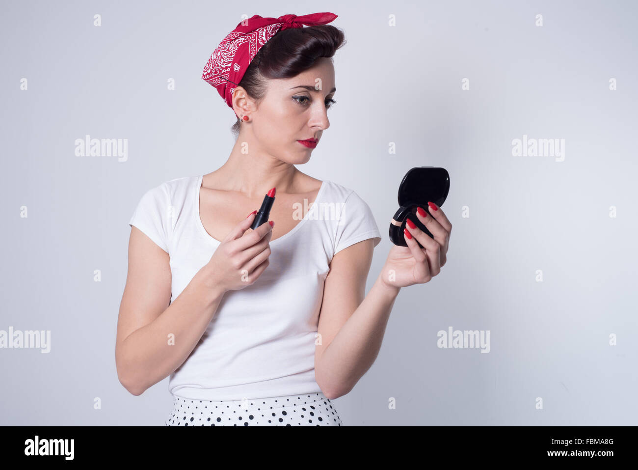 Retro pin up girl applying lipstick looking in hand mirror Stock Photo