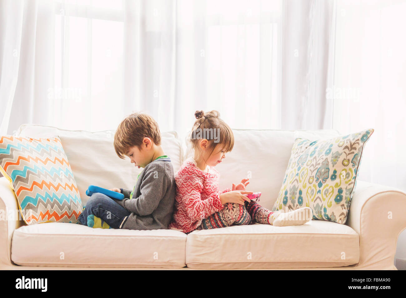 Boy and girl sitting back to back using digital tablets Stock Photo