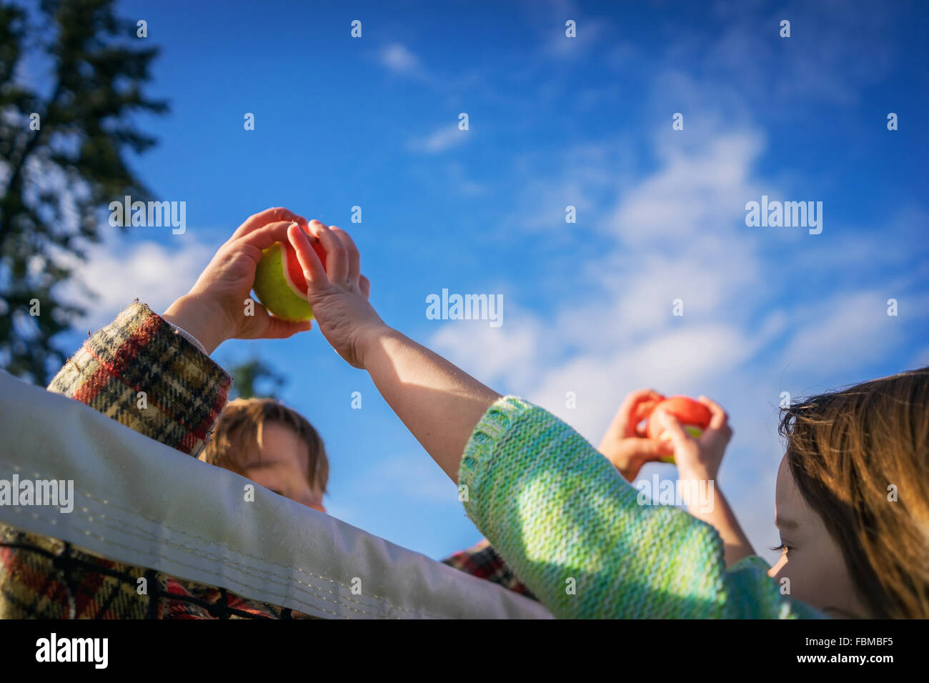 Two children passing tennis balls over the top of the net Stock Photo