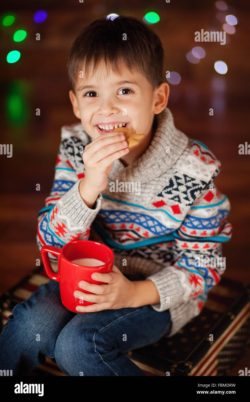 Smiling boy holding cup of milk and eating a cookie Stock Photo