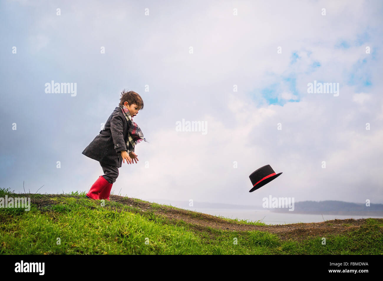 Boy chasing his hat blowing away in the wind Stock Photo