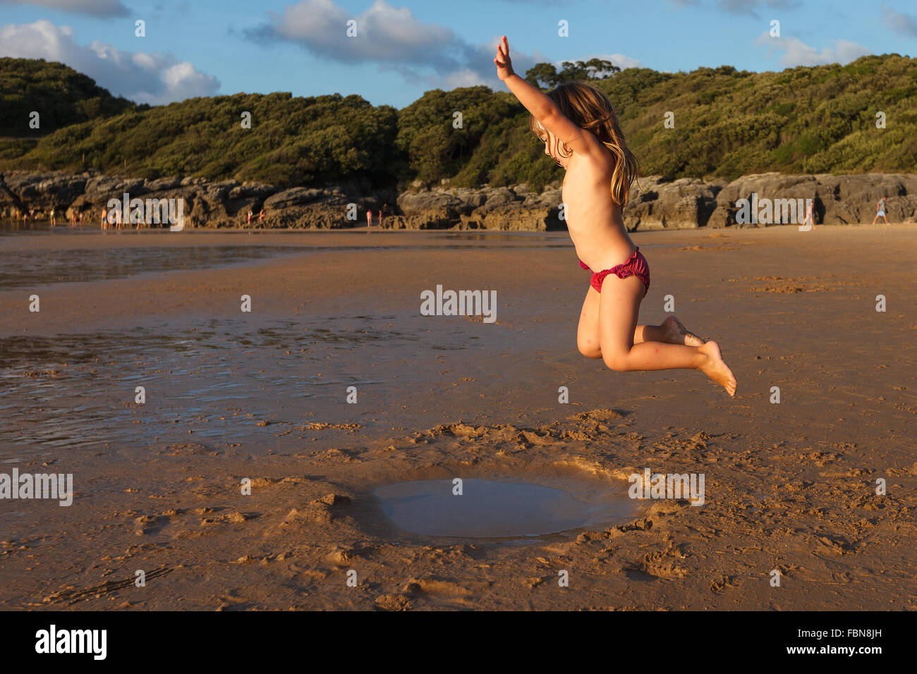 A girl jumping by the shoreline, La Arena Beach, Isla, Arnuero, Cantabria, Spain. Stock Photo