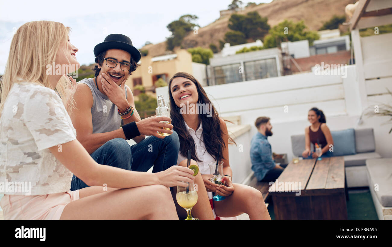 Group of friends holding drink and chatting on the roof. Young people hanging out on rooftop and  having party. Stock Photo
