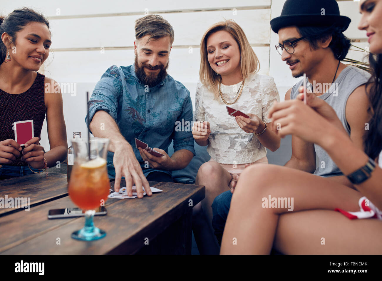 Group of friends relaxing and playing cards together. Young people hanging out together around a table during a party playing a Stock Photo