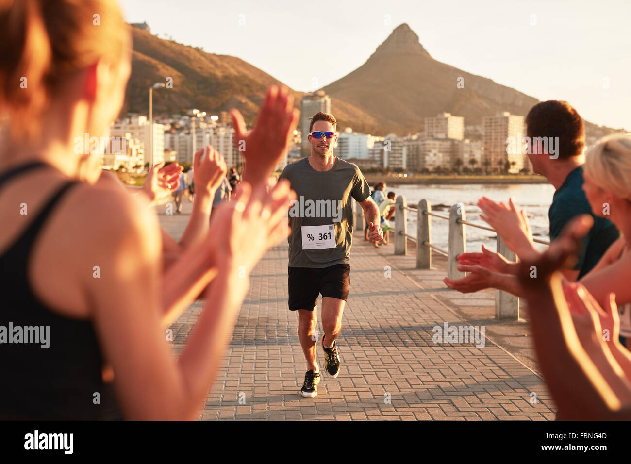 Young male athlete being applauded by supporters as he reaches the finishing line of a running race. Young people encouraging ra Stock Photo