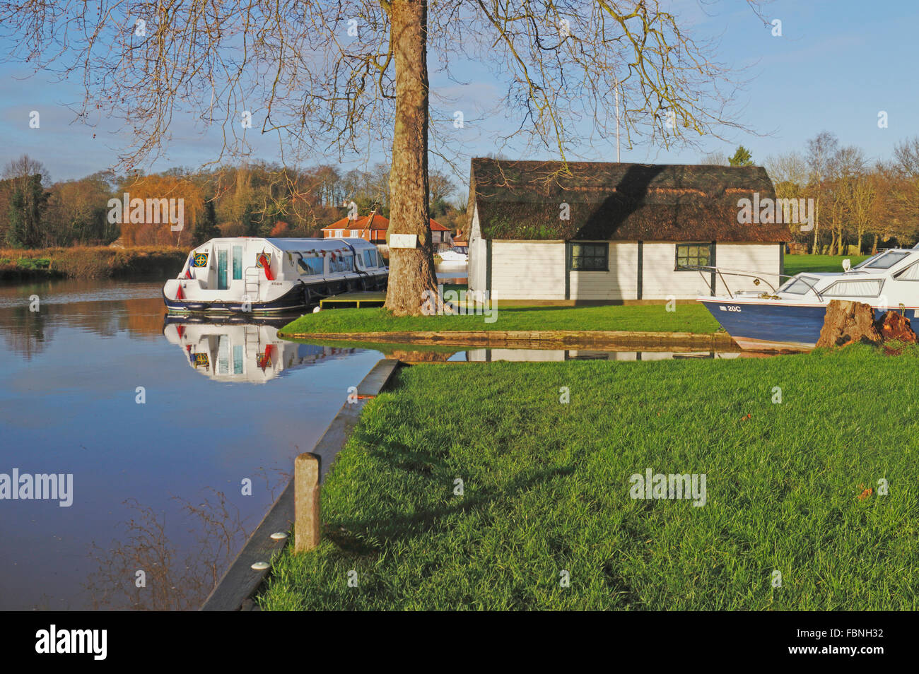 A moored cruiser and boathouse by the River Bure on the Norfolk Broads at Coltishall, Norfolk, England, United Kingdom. Stock Photo