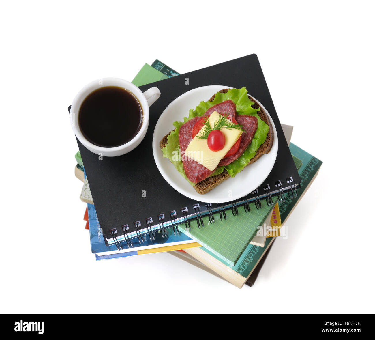 A stack of books and notebooks with a cup of coffee and a sandwich upstairs isolated Stock Photo