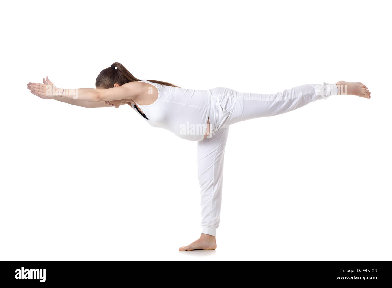 Full length portrait of young pregnant fitness model in white sportswear doing yoga or pilates training, standing in Warrior III Stock Photo